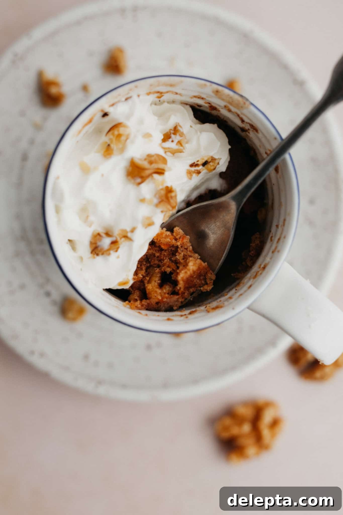 Warm Spiced Carrot Mug Delight 5 A close-up, overhead shot of a freshly microwaved carrot mug cake, beautifully adorned with a generous swirl of whipped cream and a few scattered walnut pieces.