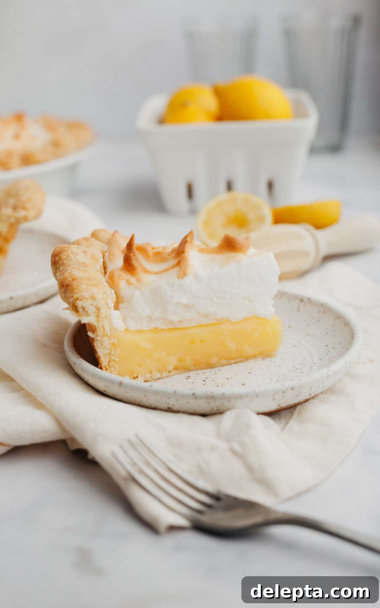 Lemon Cloud Dream 12 A delectable slice of lemon meringue pie served on a small white plate, ready to be enjoyed.