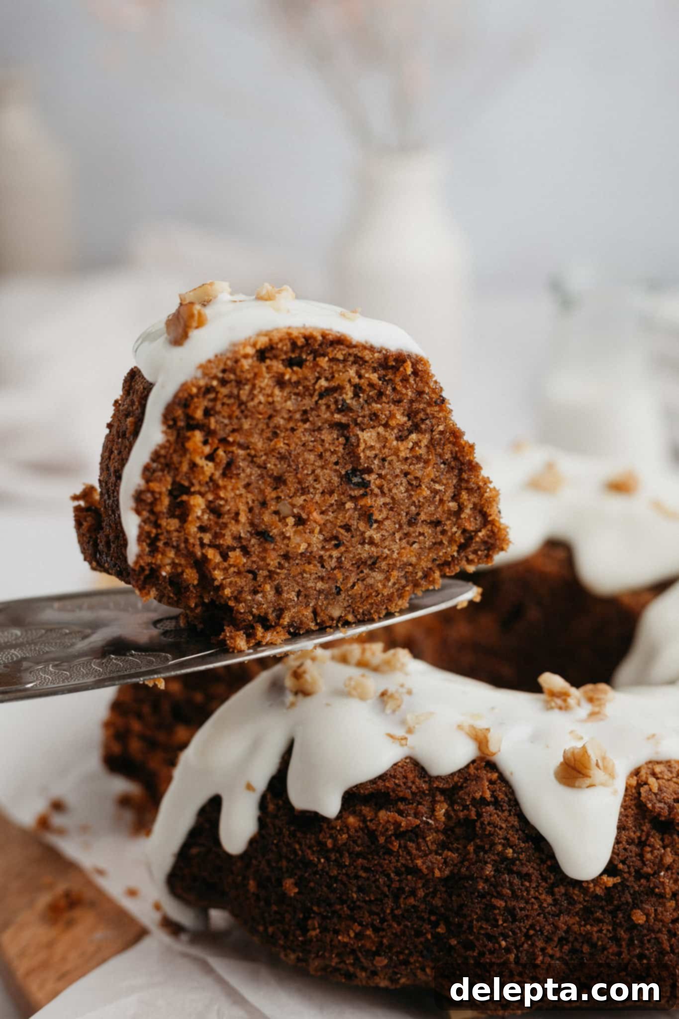 Golden Spiced Carrot Crown 7 A delectable slice of carrot bundt cake being gently lifted from the whole cake with a silver cake server, highlighting its rich texture and glaze.