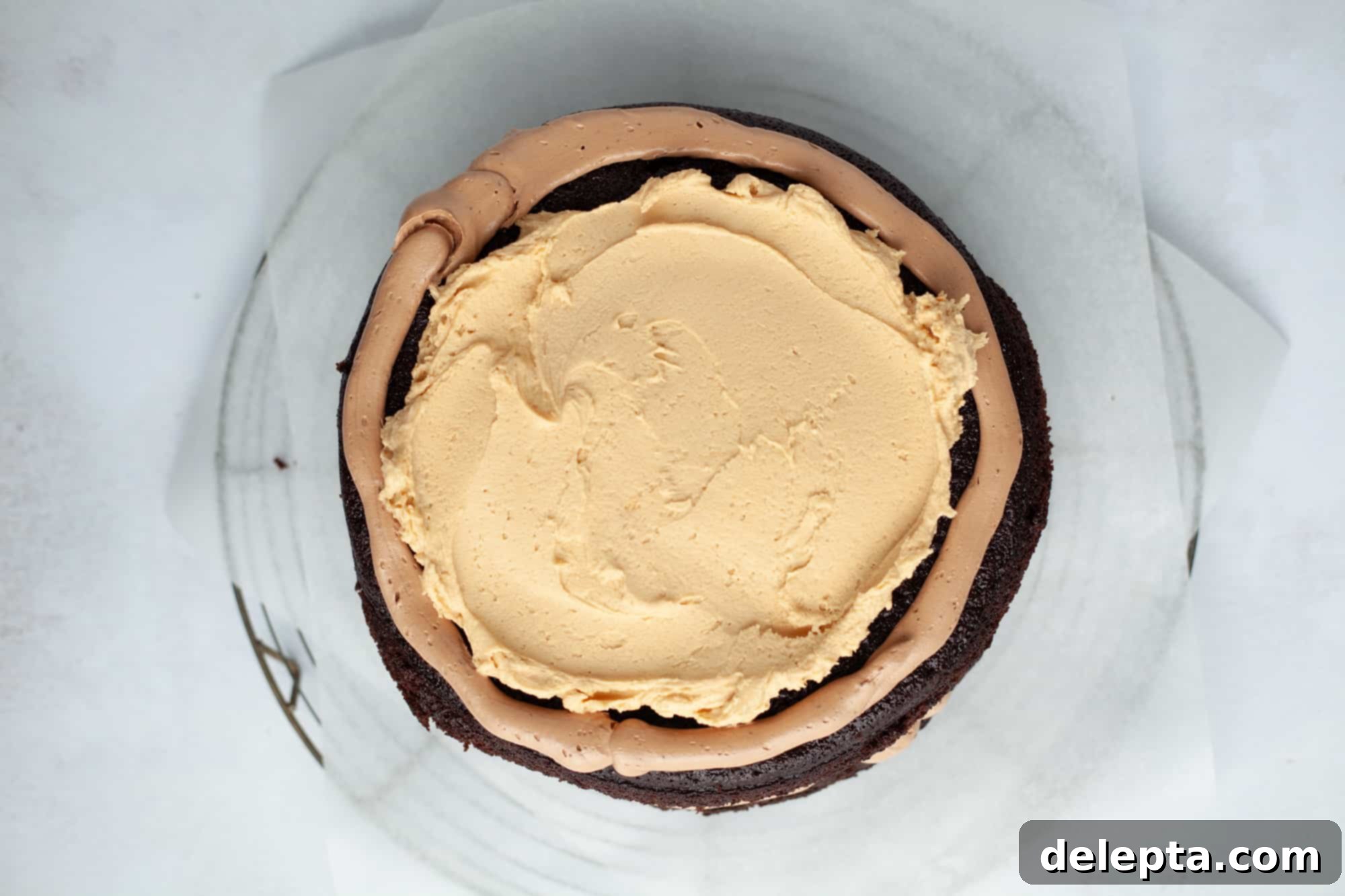 Peanut Butter Chocolate Nirvana 15 An overhead shot of a chocolate cake on parchment paper. The cake has an outer ring of chocolate frosting, and the middle is filled with a peanut butter filling
