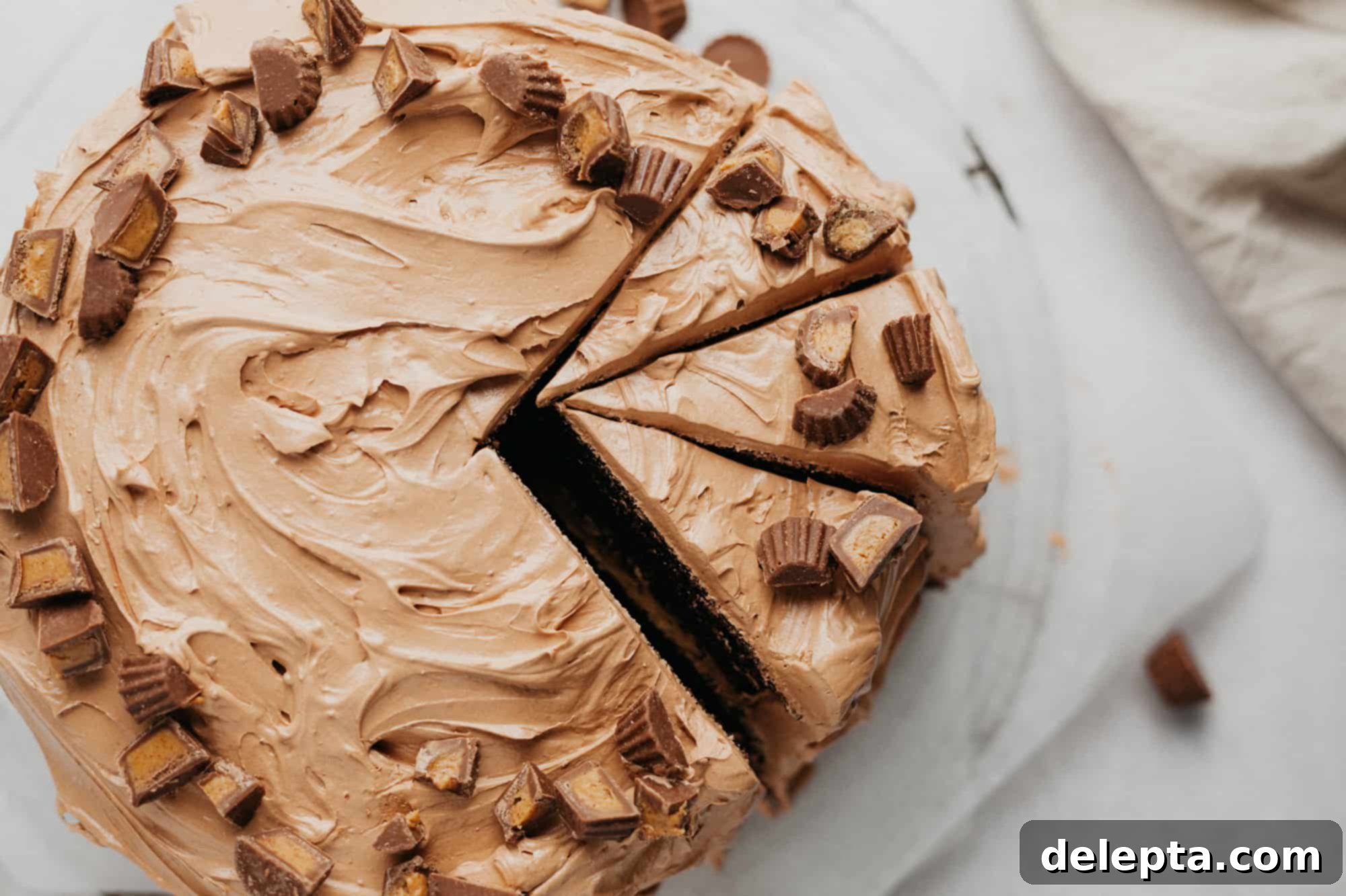 Peanut Butter Chocolate Nirvana 18 An overhead shot of a chocolate frosted cake with miniature peanut butter cups along the outside edge. Three slices have been cut