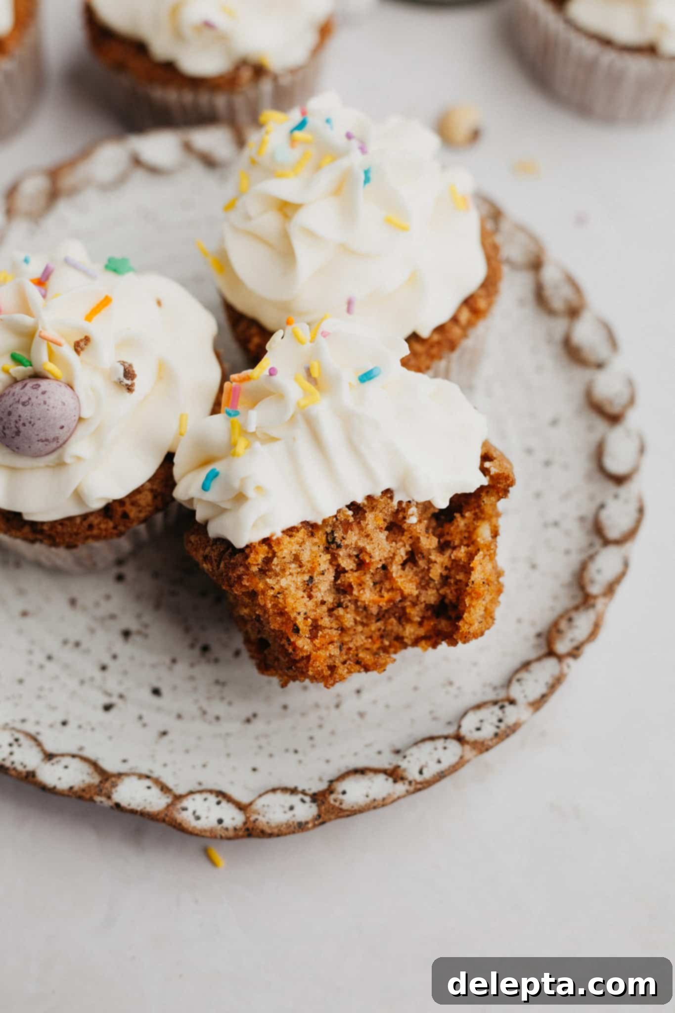 Carrot Cake Cupcakes with Cream Cheese Frosting 2 A small plate with three carrot cupcakes, one has a bite taken out of it.