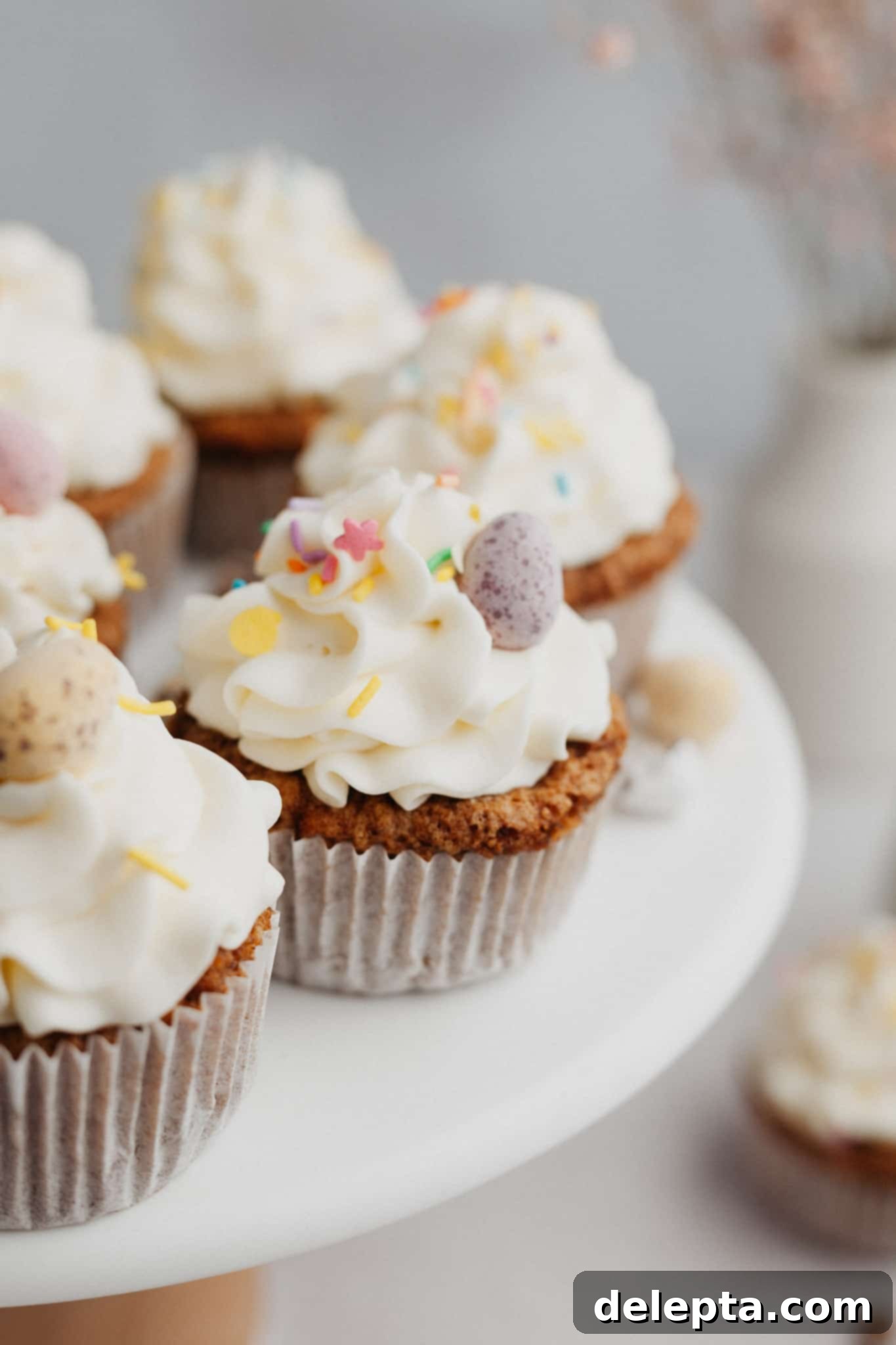 Carrot Cake Cupcakes with Cream Cheese Frosting 8 Several carrot cupcakes with white frosting on a cake stand.