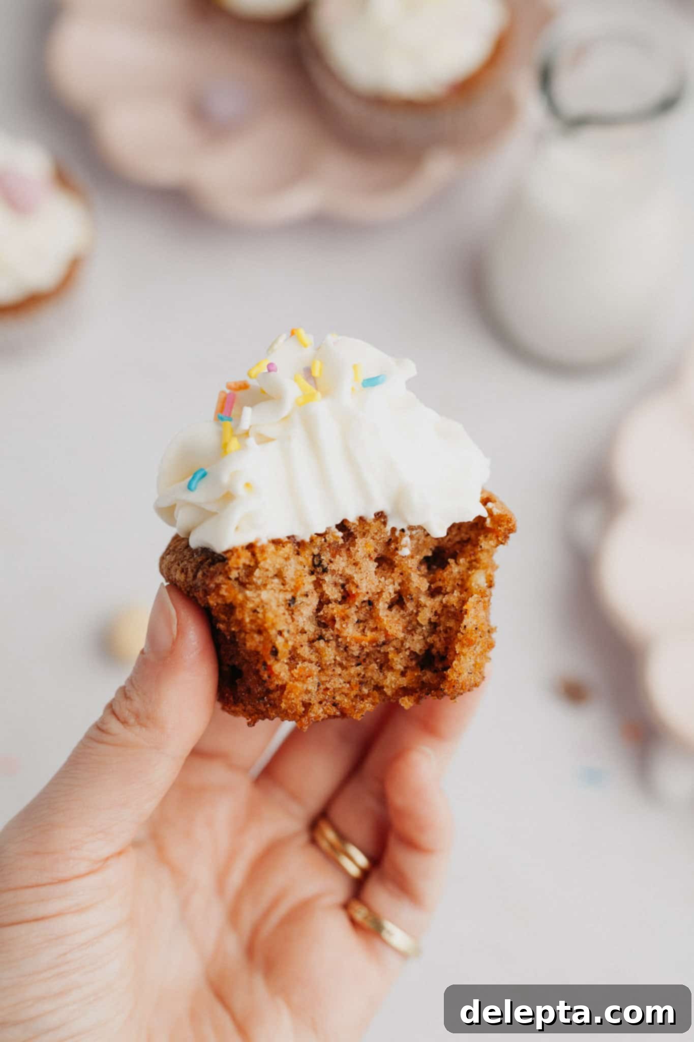 Carrot Cake Cupcakes with Cream Cheese Frosting 9 A hand holding a carrot cupcake with a bite taken out of it.