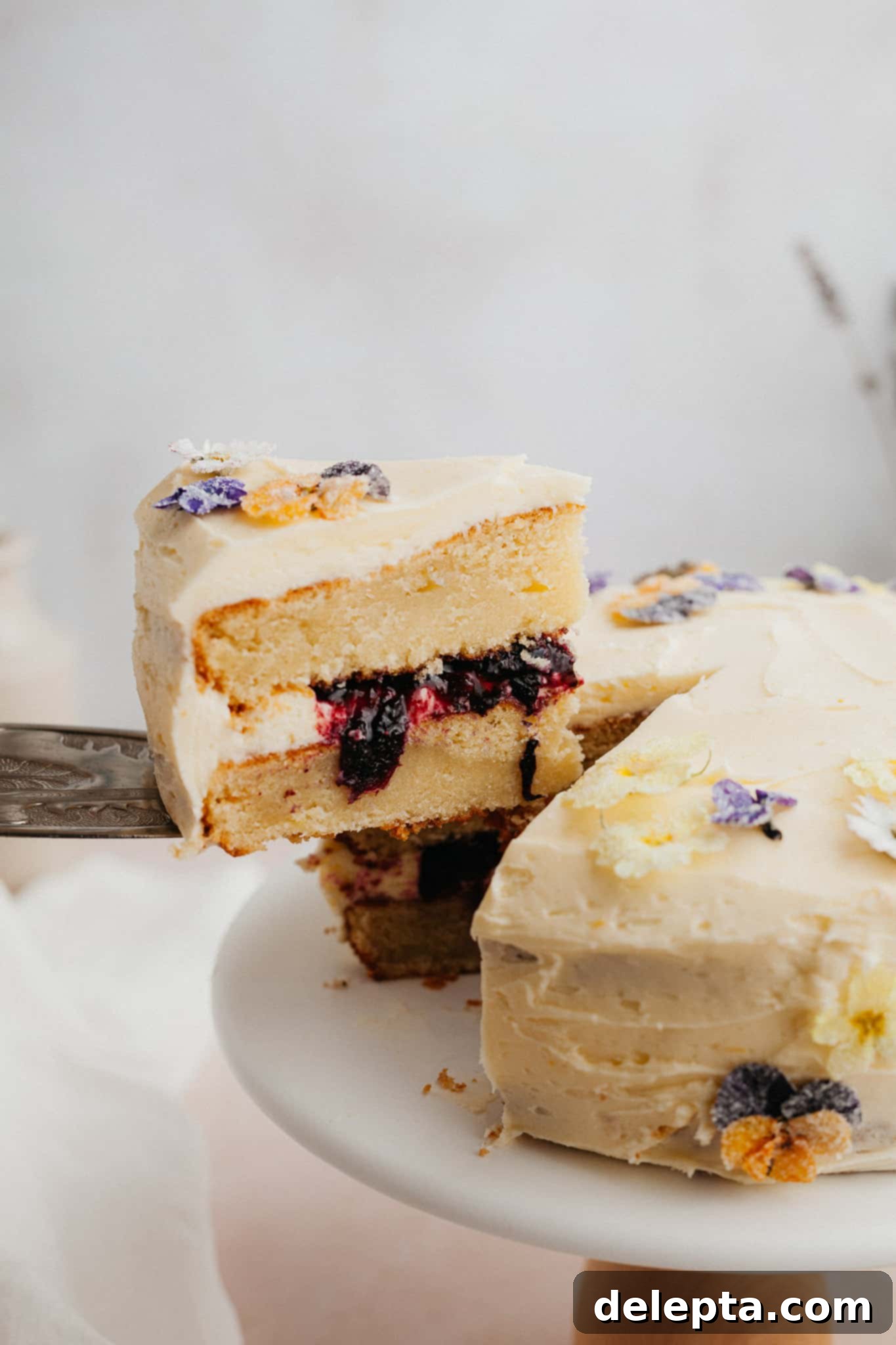 Zesty Lemon Blueberry Layer Cake 2 A stunning yellow lemon blueberry cake with a visible blueberry filling, a silver cake server carefully lifting one slice out.