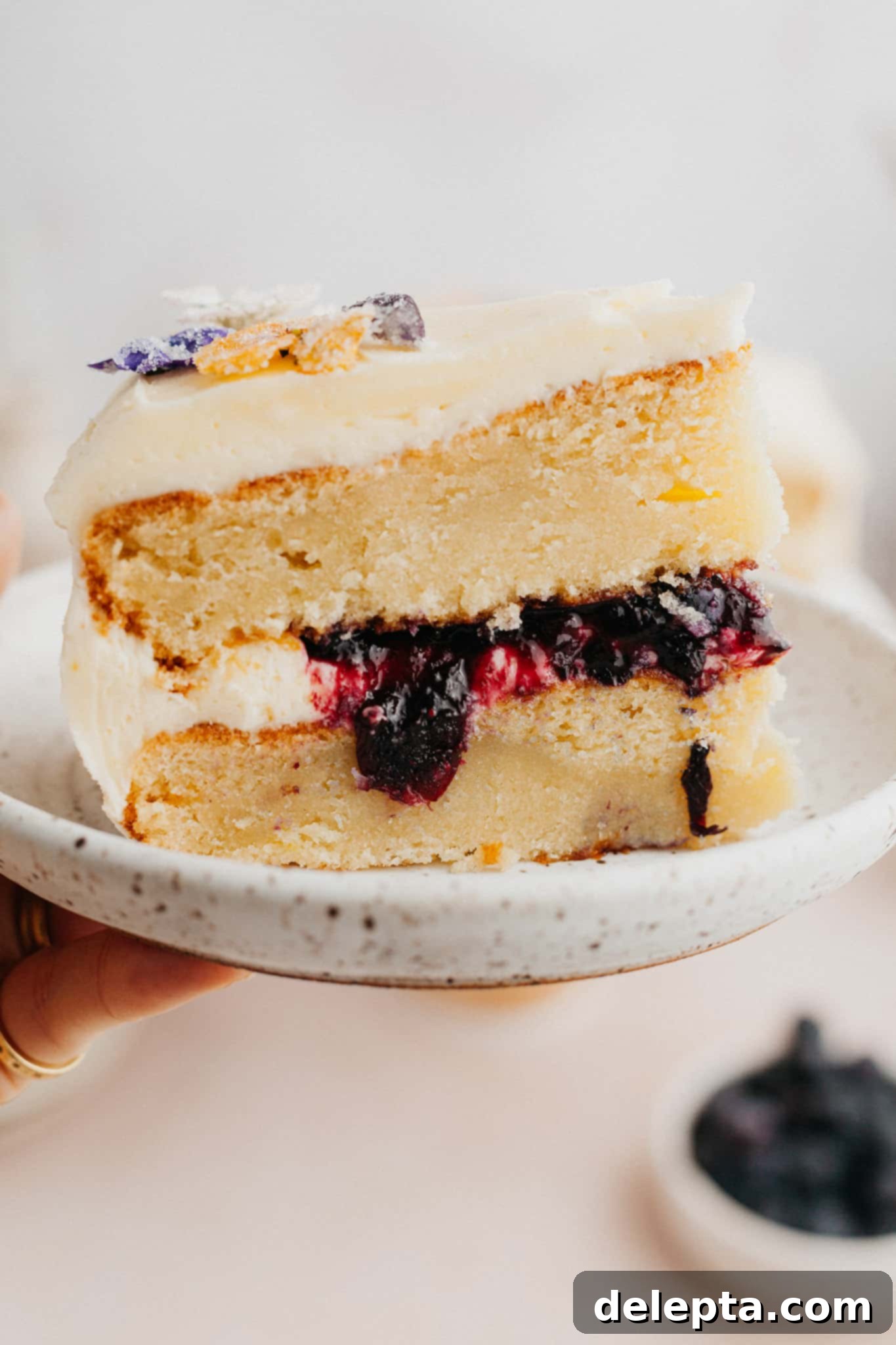 Zesty Lemon Blueberry Layer Cake 9 A perfectly sliced piece of blueberry filled lemon cake on a small white plate, showcasing the layers.