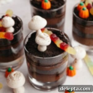 Spooky Simple Homemade Chocolate Pudding Dirt Cups 11 Glass cups with layers of chocolate pudding and Oreo cookie crumbs, decorated with meringue mushrooms and gummy worms.