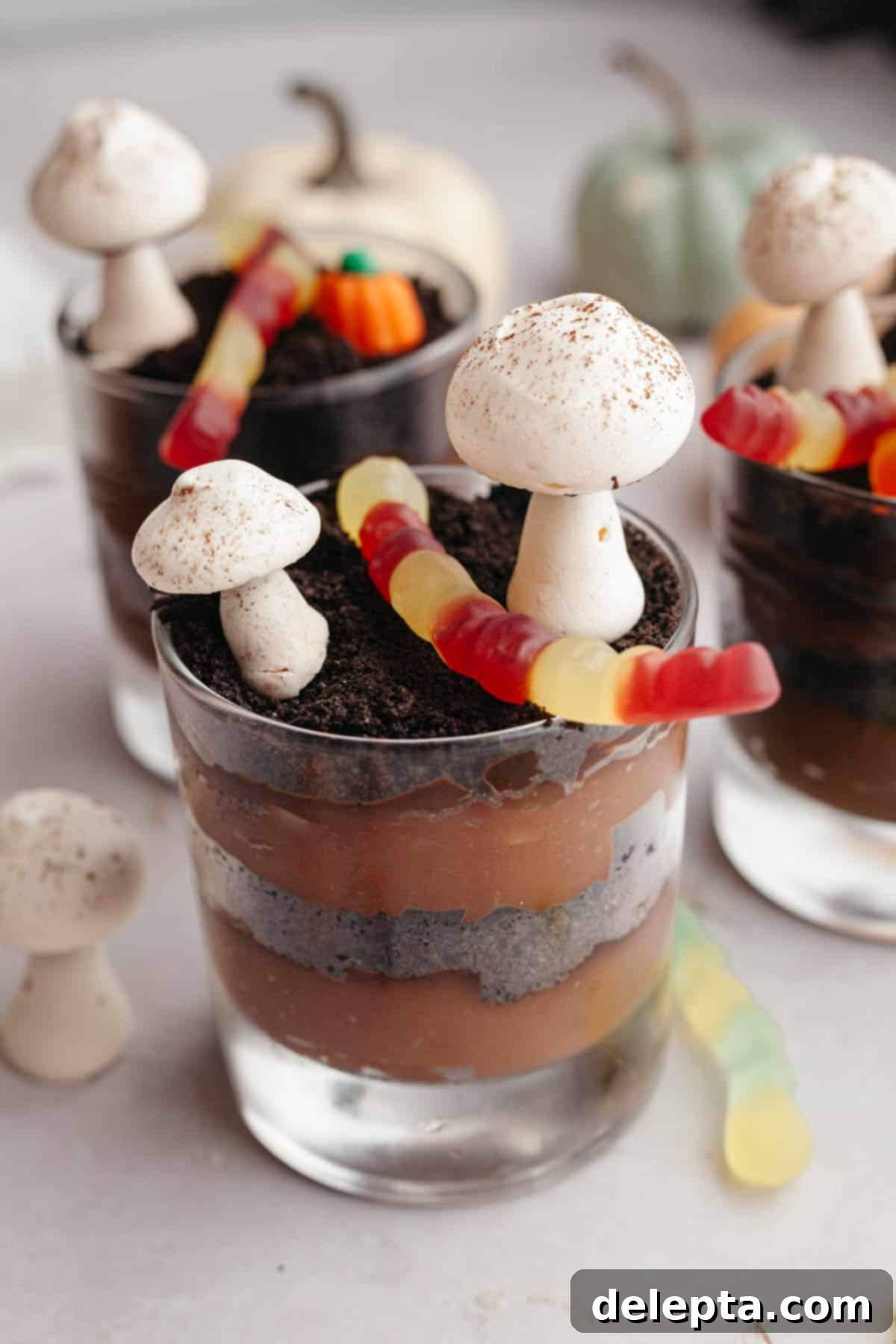 Spooky Simple Homemade Chocolate Pudding Dirt Cups 9 Glass cups with layers of chocolate pudding and Oreo cookie crumbs, decorated with meringue mushrooms and gummy worms.