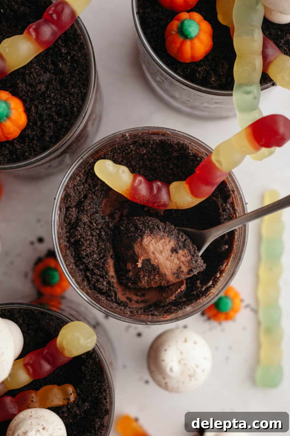 Spooky Simple Homemade Chocolate Pudding Dirt Cups 10 An overhead shot of Oreo Halloween dirt cups, decorated with gummy worms and mini mushrooms. One dirt cup has a spoon in it, showing you the pudding layer.