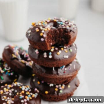 Chocolatey Sprinkled Delights 9 A stack of chocolate sprinkle donuts, the donut on top has a bite taken out of it, showcasing its fluffy texture and inviting glaze.