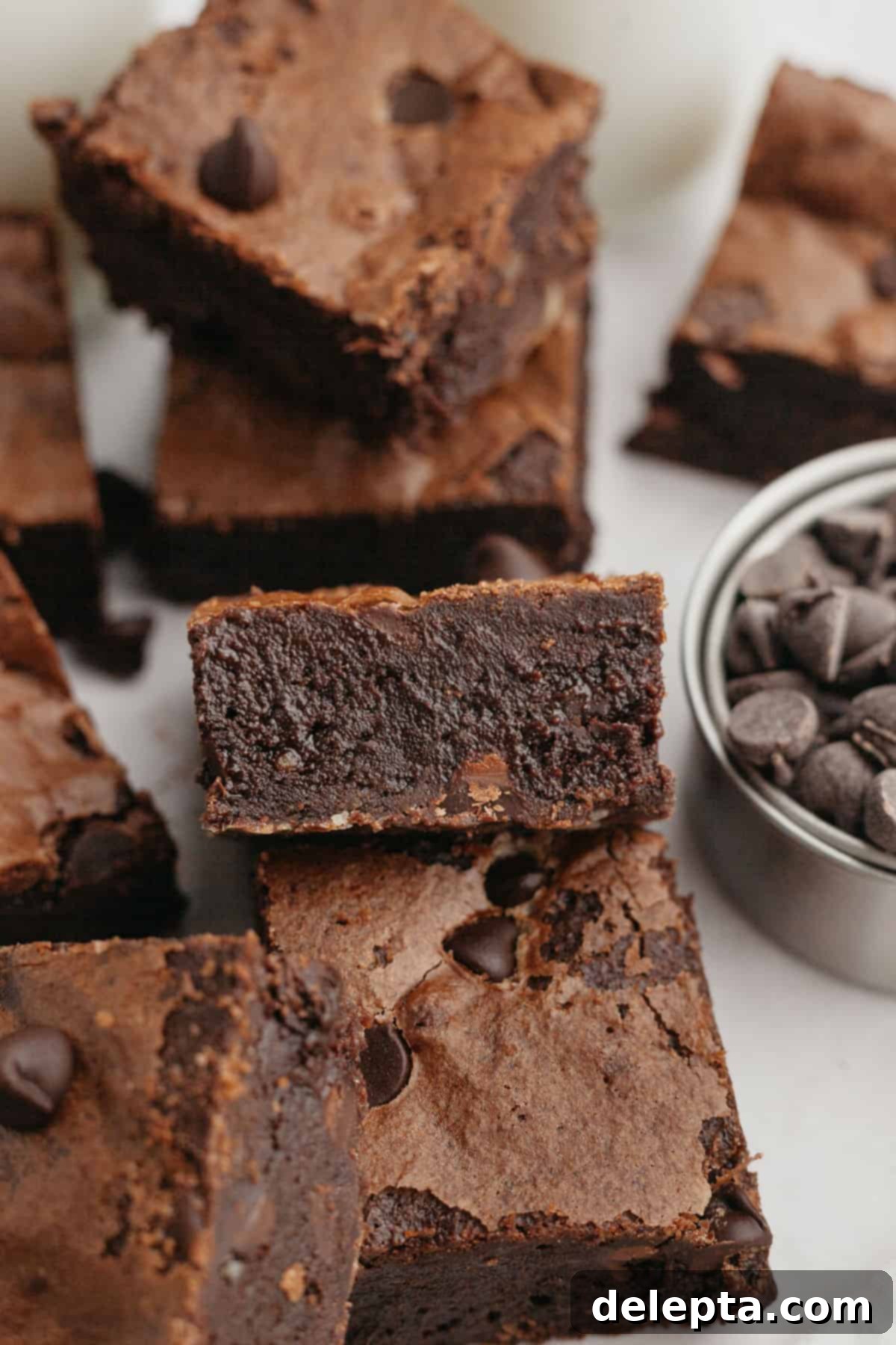 Decadent Fudgy Triple Chocolate Brownies 2 Perfectly baked triple chocolate brownies resting on parchment paper, showcasing their enticing crackle top and rich texture.