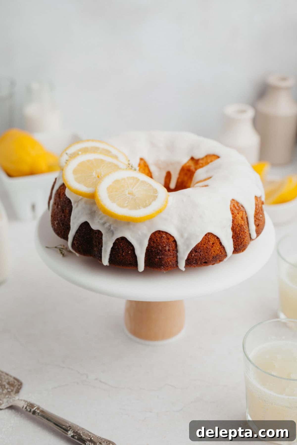 Sunny Lemon Bundt Bliss 2 A beautifully glazed lemon bundt cake adorned with fresh lemon slices, presented on an elegant white cake stand.