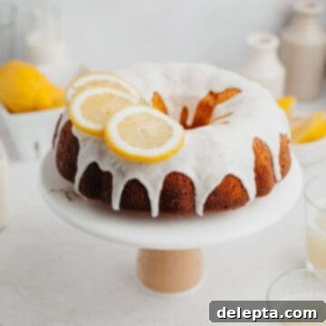 Sunny Lemon Bundt Bliss 9 A lemon bundt cake covered in a white glaze and slices of lemon on a white cake stand, showcasing its delicious appeal.