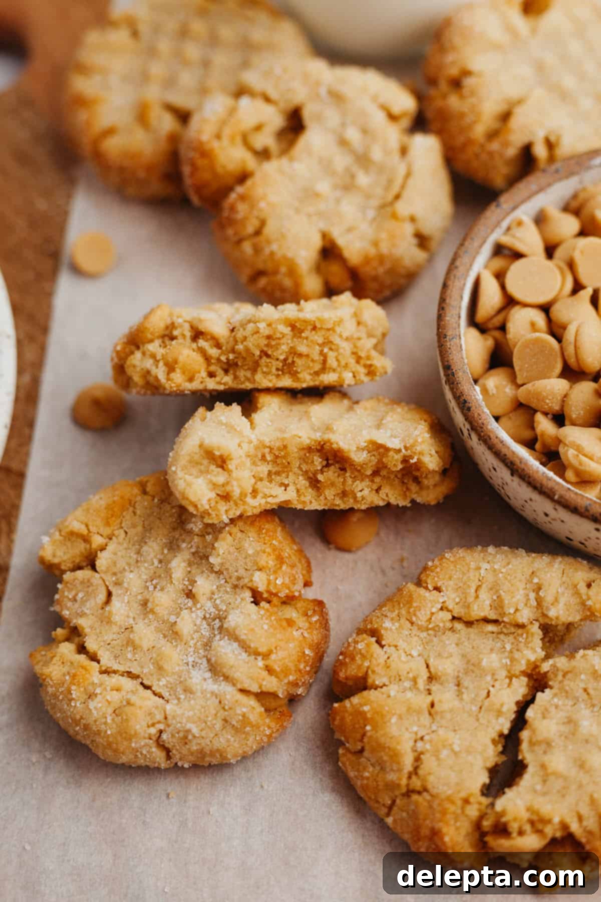 Peanut Butter Bliss in a Small Batch 2 Several golden brown, soft peanut butter cookies on parchment paper, with one cookie thoughtfully cut in half to showcase its delightful chewy interior. The two halves are stacked invitingly.