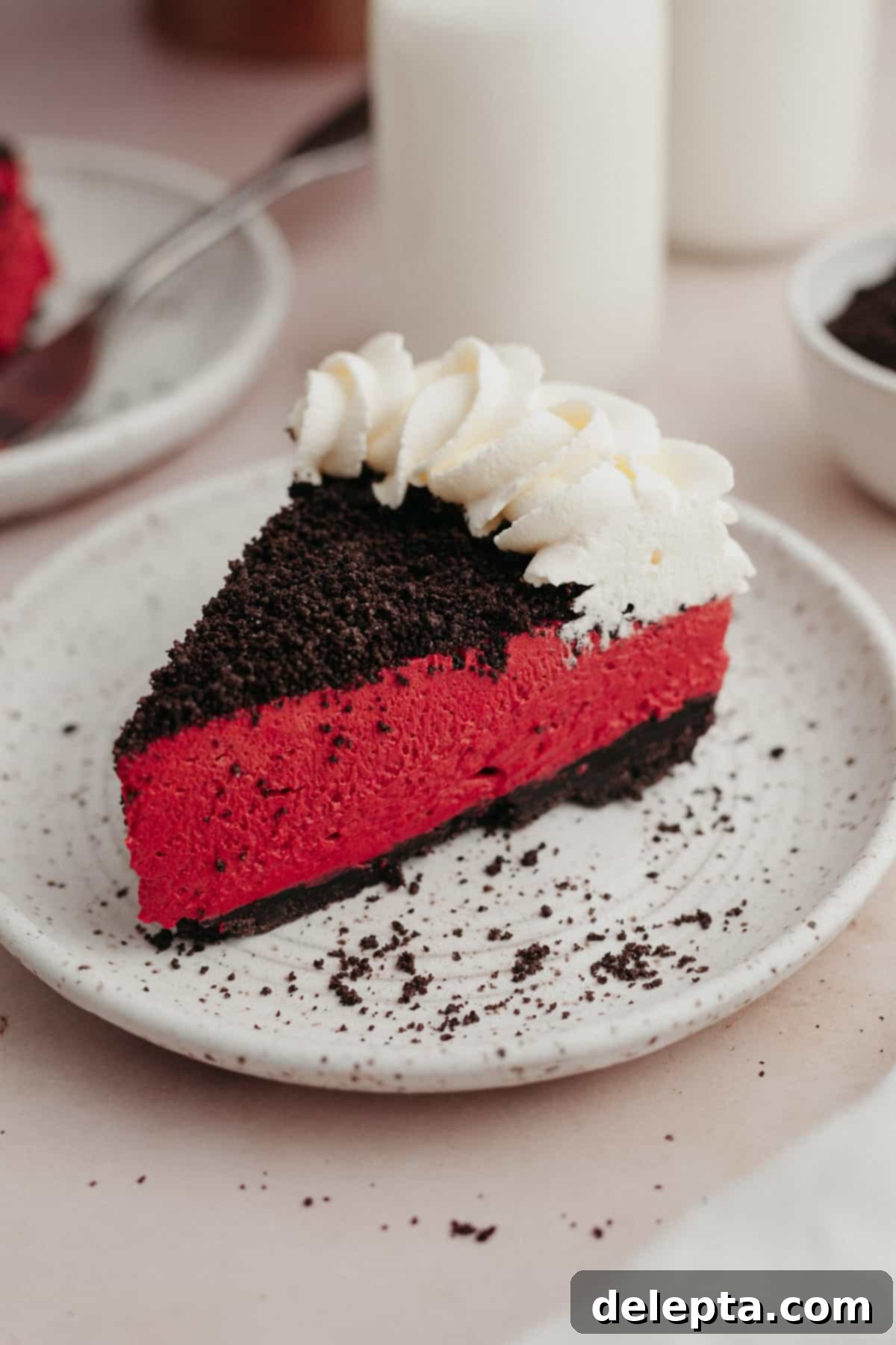 Decadent No-Bake Red Velvet Oreo Cheesecake 2 A perfectly sliced piece of red velvet oreo cheesecake on a small white plate, showcasing its vibrant layers.