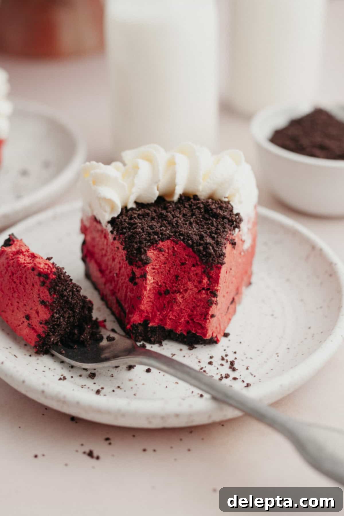Decadent No-Bake Red Velvet Oreo Cheesecake 8 A delectable slice of Oreo red velvet cheesecake on a small plate with a bite already taken out, highlighting its rich layers.
