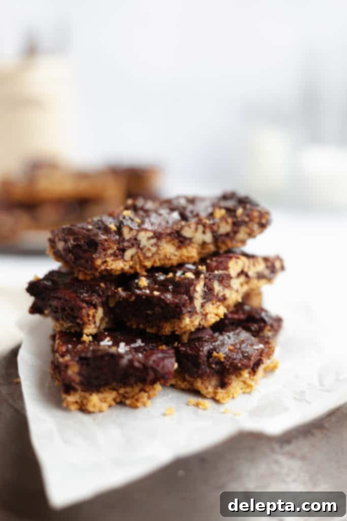Decadent Chocolate Pecan Pie Bars 2 chocolate pecan pie bars cut and stacked on top of parchment paper, showcasing their rich filling and shortbread base