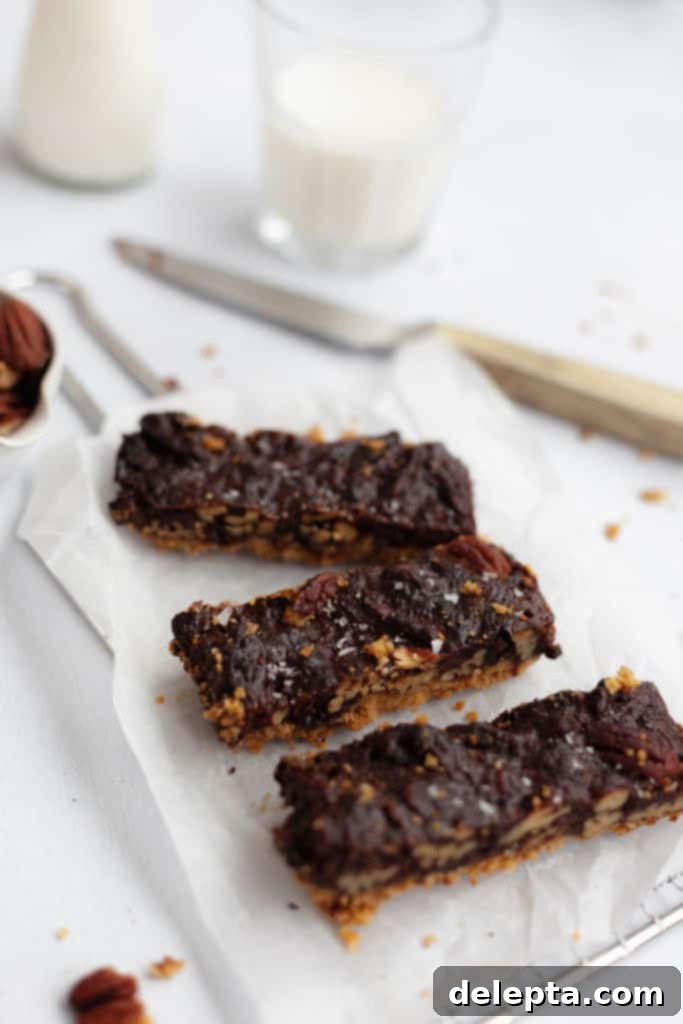 Decadent Chocolate Pecan Pie Bars 5 three chocolate pecan pie bars on parchment paper, showing the rich filling and flaky crust