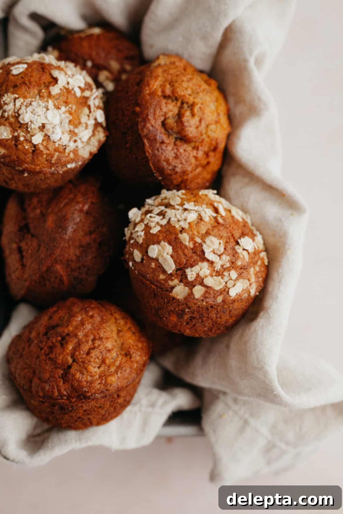 Sunshine Carrot Banana Muffins 6 A light brown linen in a loaf pan, it is filled with muffins which are topped with oats.