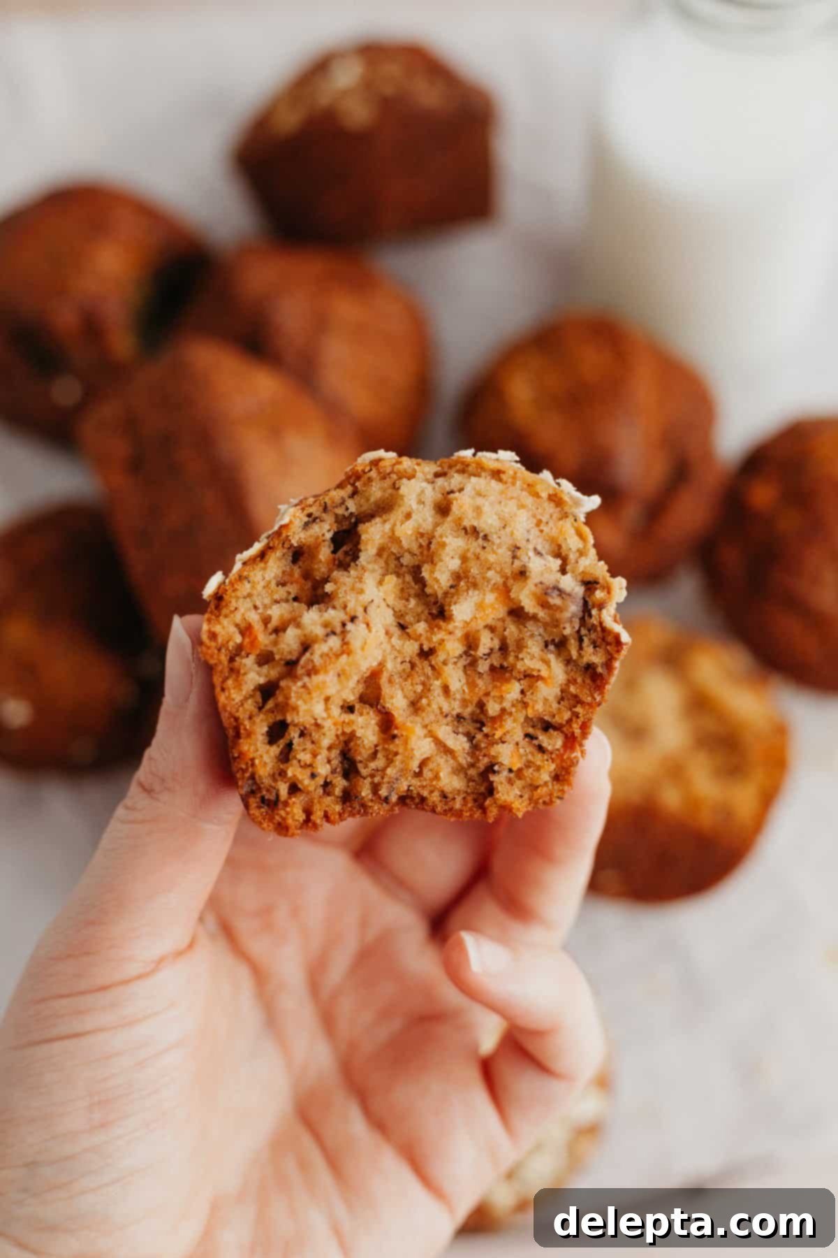 Sunshine Carrot Banana Muffins 7 A hand holding a moist banana carrot muffin cut in half, showing the tender crumb and carrot flecks.