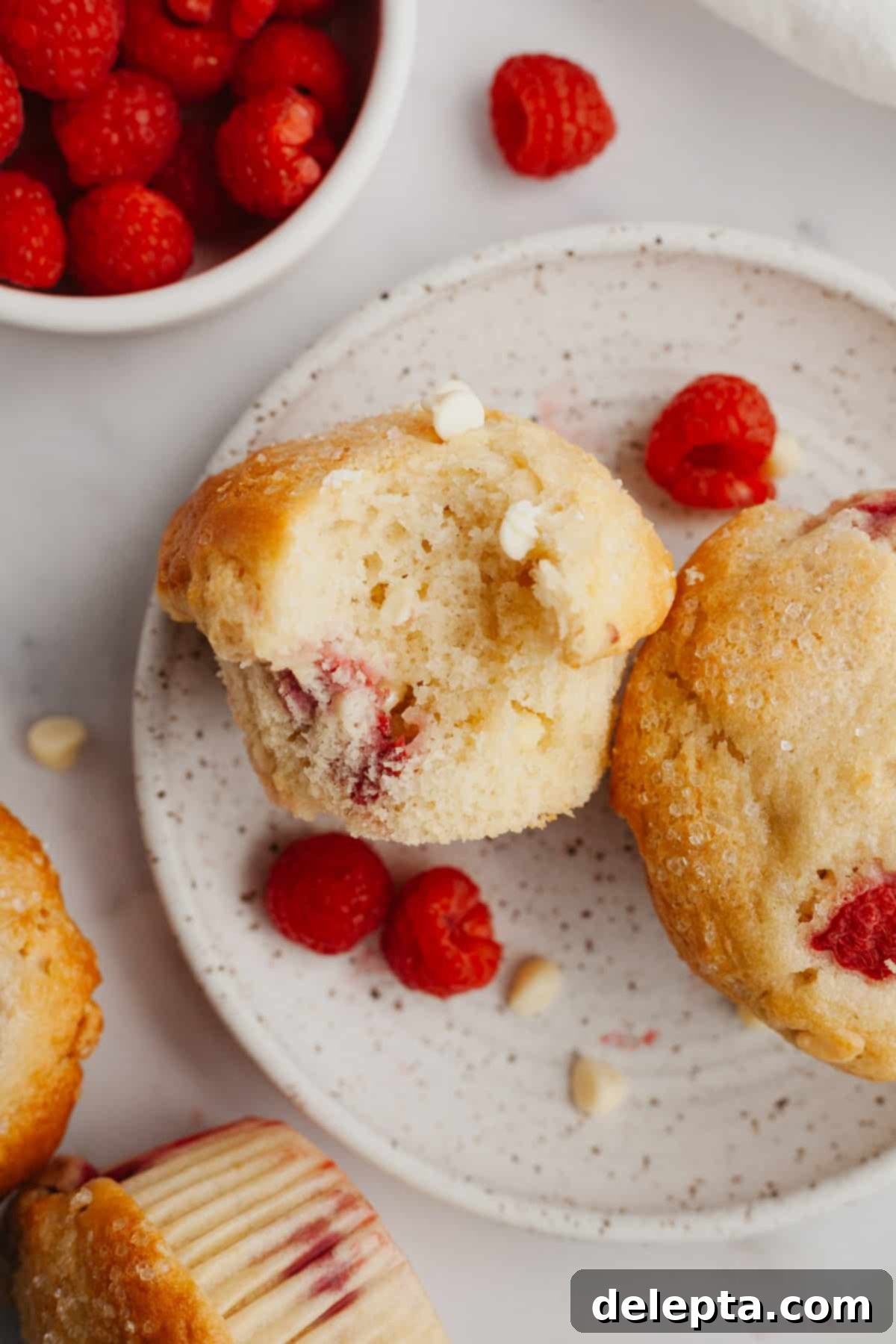 Decadent Raspberry White Chocolate Muffins 2 A perfectly baked raspberry white chocolate muffin with a bite taken out, revealing the fluffy interior and fruit.