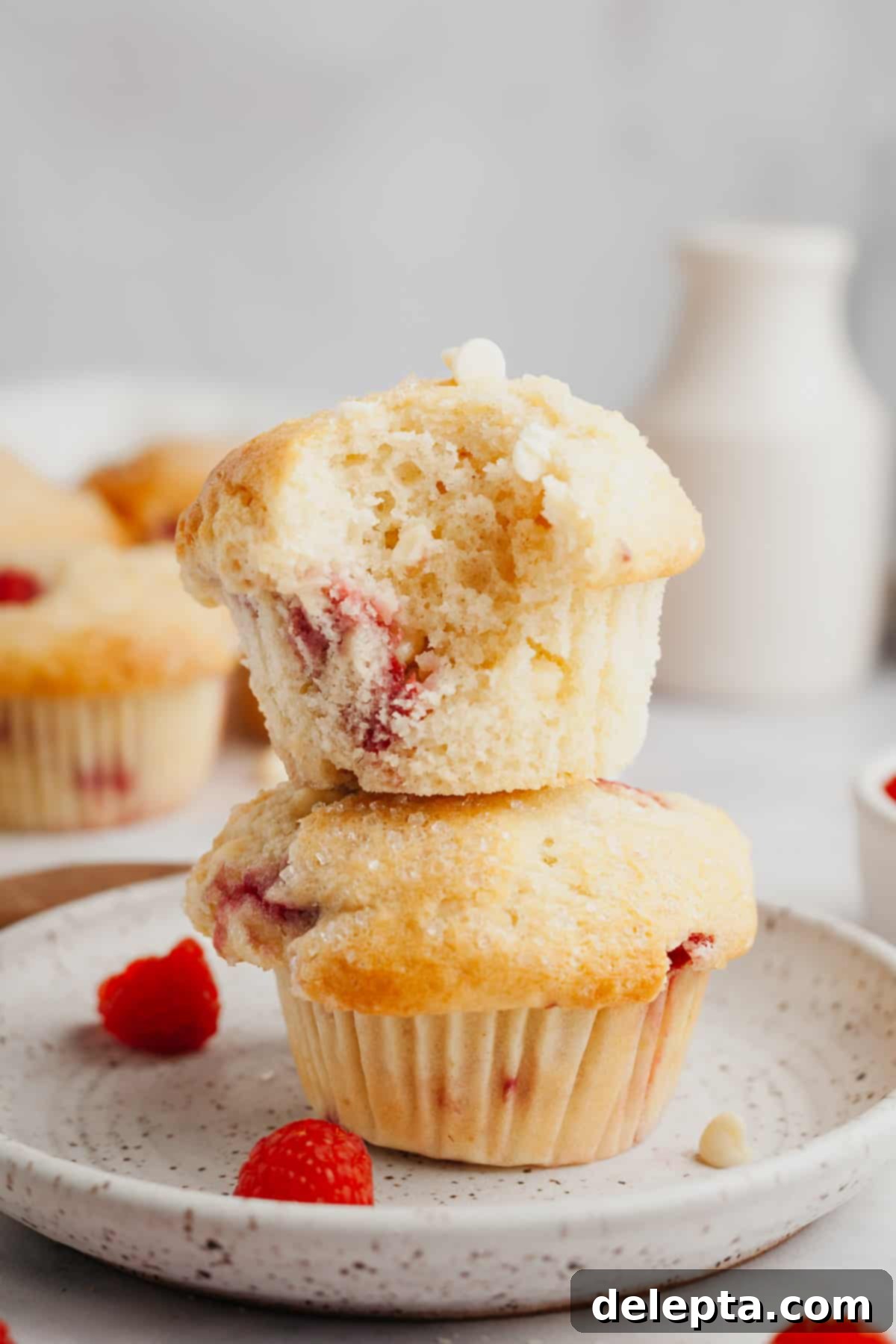 Decadent Raspberry White Chocolate Muffins 7 A stack of two perfectly golden-brown raspberry white chocolate muffins on a wire rack.
