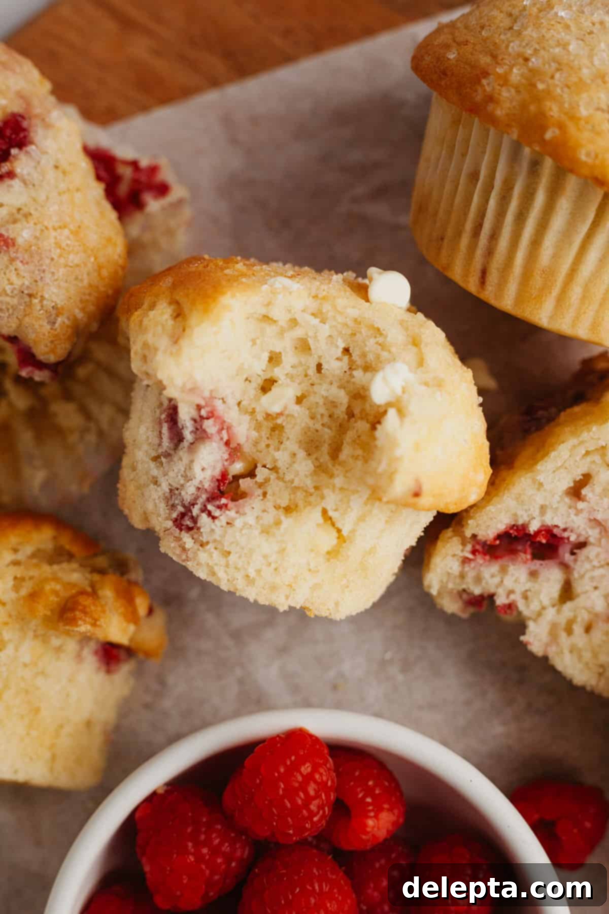 Decadent Raspberry White Chocolate Muffins 8 A single raspberry white chocolate muffin on a piece of parchment paper, with a bite taken out to show its fluffy texture.