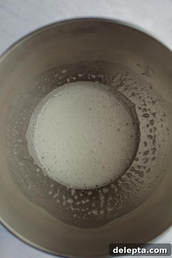 Cookies & Cream Macarons 5 Egg whites and granulated sugar are being gently whisked over a double boiler in a large silver mixing bowl, preparing to create the meringue base.