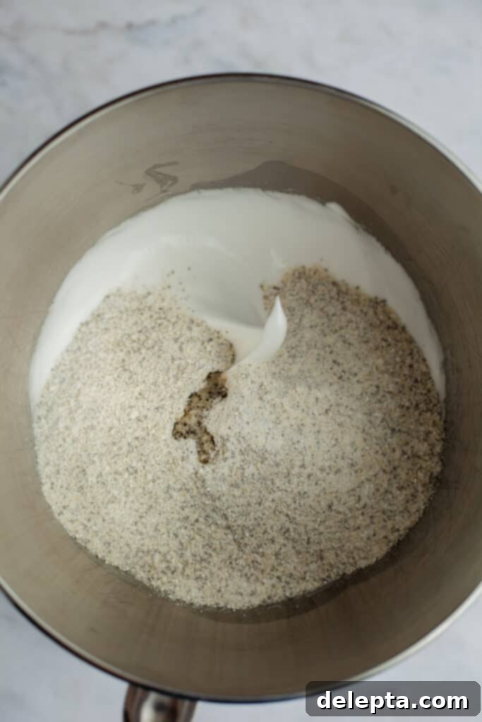 Cookies & Cream Macarons 7 The fluffy white meringue is topped with the finely ground almond mixture in a silver mixing bowl, preparing for the macaronage stage.