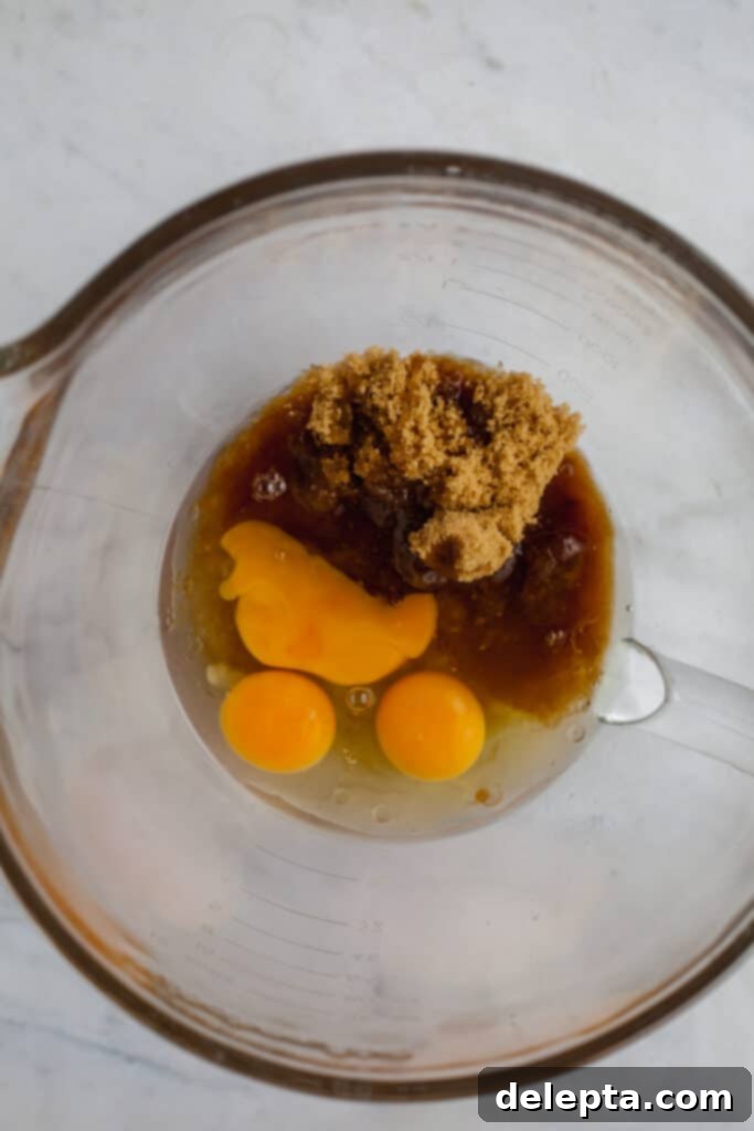 Fudgy Brownie Pie 13 A large clear glass bowl filled with a combination of eggs, neutral oil, fragrant vanilla extract, and a blend of both granulated and brown sugars, meticulously prepared and ready to be whisked for the brownie batter.