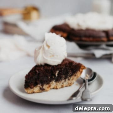 Fudgy Brownie Pie 19 A perfectly baked slice of brookie pie, showcasing its rich fudgy brownie layer and chewy cookie crust, elegantly topped with a dollop of fresh whipped cream and served on a small, charming plate.