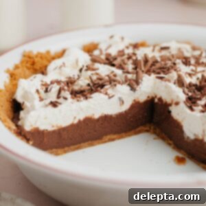 No-Bake Chocolate Pudding Pie with Buttery Graham Crust 10 A chocolate pudding pie covered in whipped cream in a white pie dish.