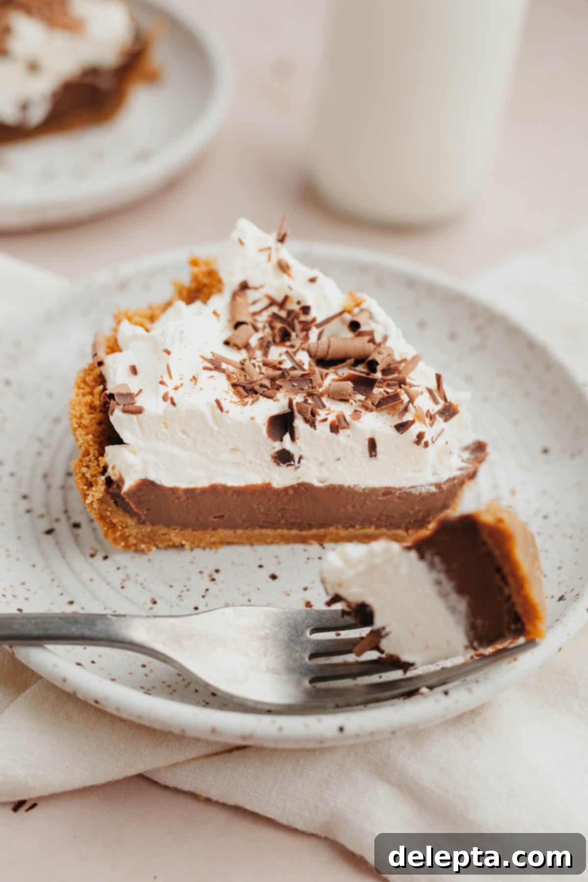 No-Bake Chocolate Pudding Pie with Buttery Graham Crust 9 A slice of chocolate pudding pie topped with whipped cream on a small speckled plate.
