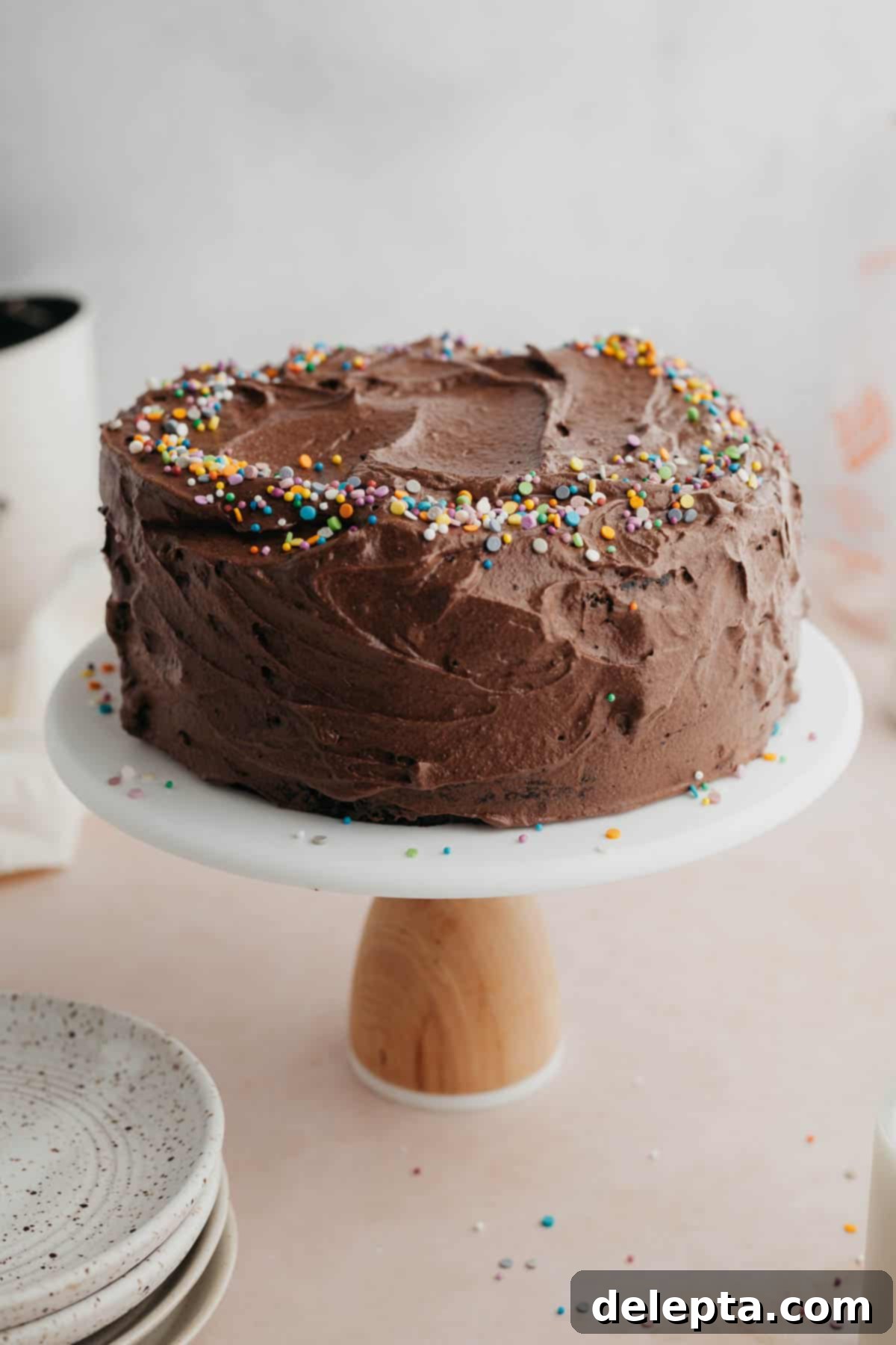 Velvet Chocolate Cream Cheese Delight 9 A beautifully frosted chocolate cake with chocolate cream cheese frosting and rainbow sprinkles, presented on a white cake stand.