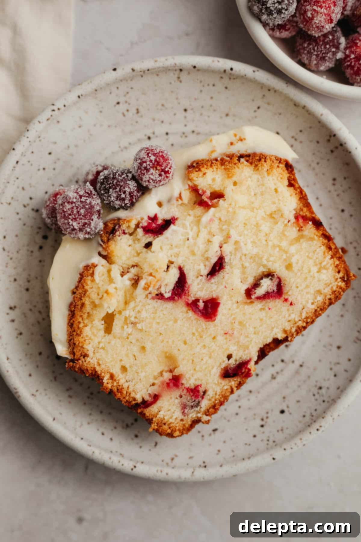 Lemon-Kissed Cranberry Loaf with White Chocolate Embrace 11 A perfectly sliced piece of moist cranberry lemon bread, showcasing its tender crumb and a generous swirl of white chocolate cream cheese frosting on a small, elegant plate.