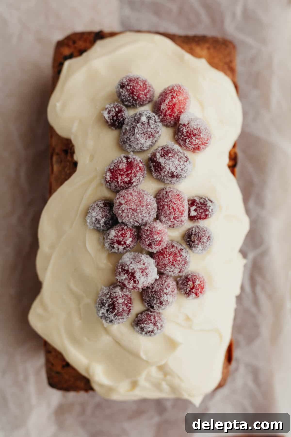 Lemon-Kissed Cranberry Loaf with White Chocolate Embrace 10 An inviting overhead shot of a fully frosted cranberry lemon bread loaf, beautifully decorated with a neat row of glistening sugared cranberries, ready to be sliced and served.