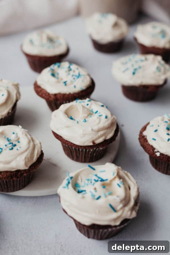 Hanukkah's Golden Glow: Chocolate, Salted Caramel & Tahini Buttercream Cupcakes 2 Ten Hanukkah chocolate cupcakes generously frosted with light tahini buttercream and adorned with festive blue and white sprinkles, arranged on a rustic wooden surface, ready for celebration