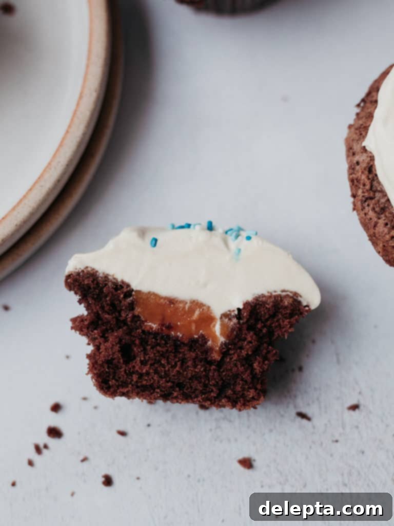 Hanukkah's Golden Glow: Chocolate, Salted Caramel & Tahini Buttercream Cupcakes 3 A chocolate cupcake sliced in half, revealing a glistening salted caramel filling nestled in its core, with a delicate tahini frosting on top, showcasing the delicious 'gelt' surprise