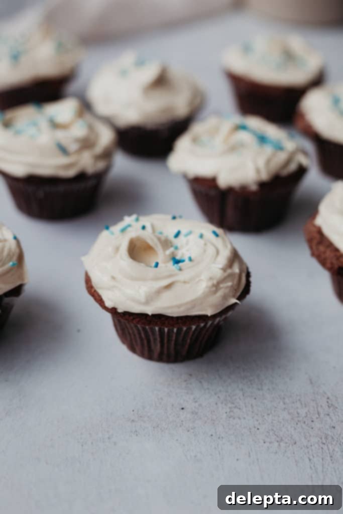 Hanukkah's Golden Glow: Chocolate, Salted Caramel & Tahini Buttercream Cupcakes 5 Four beautifully decorated chocolate cupcakes with tahini frosting and blue sprinkles, arranged closely on a light surface, ready to be enjoyed as a festive Hanukkah treat