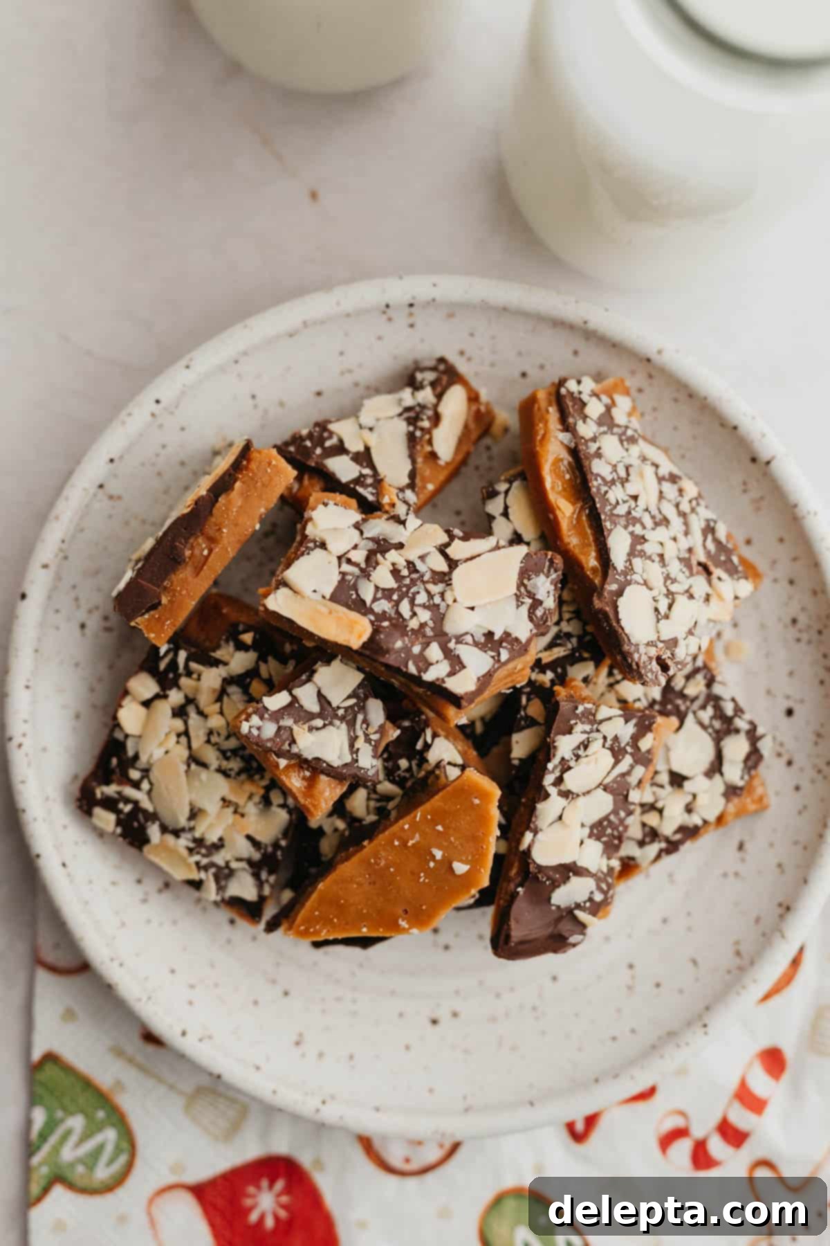 Sweet Almond Buttercrunch 2 A small plate with glistening pieces of homemade almond toffee, showcasing its crunchy texture and chocolate layer topped with toasted almonds and sea salt.