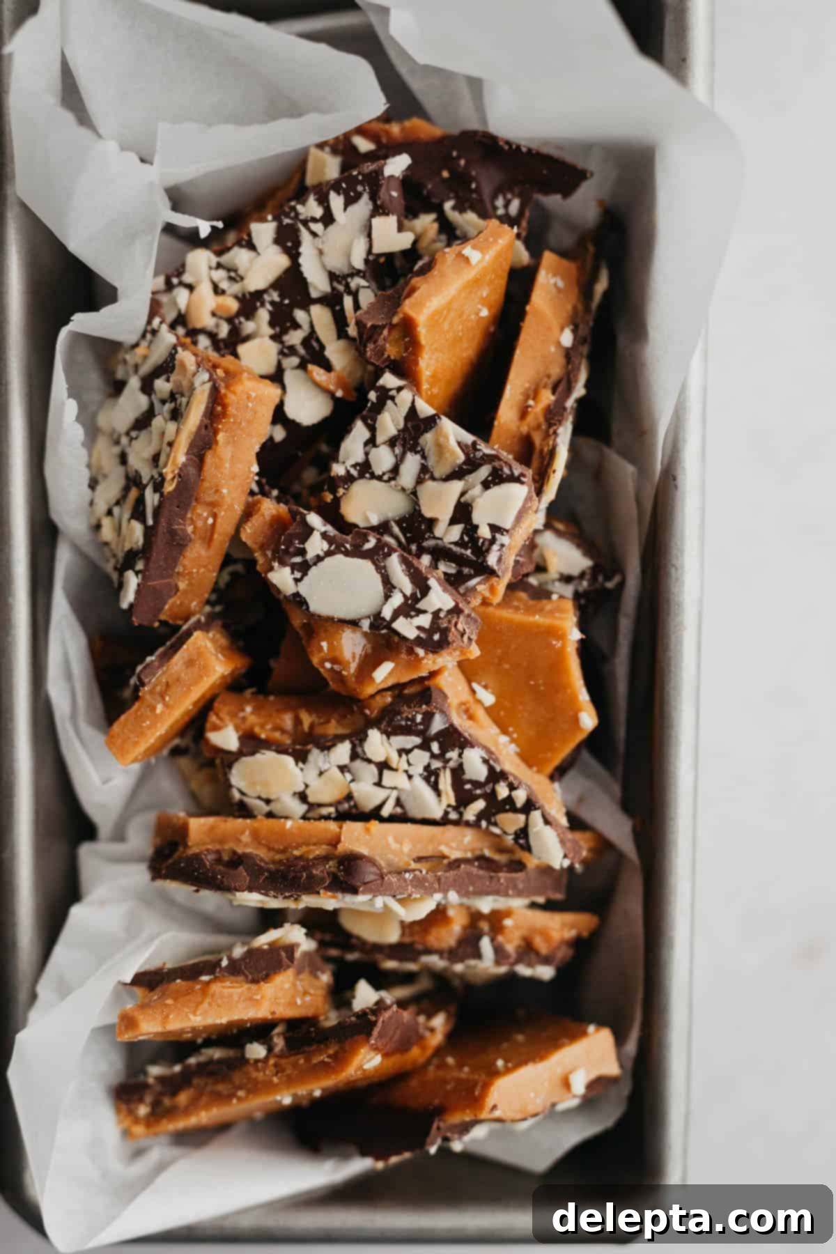Sweet Almond Buttercrunch 7 A loaf pan lined with parchment paper and filled with numerous pieces of delicious almond toffee, ready for packaging or serving.