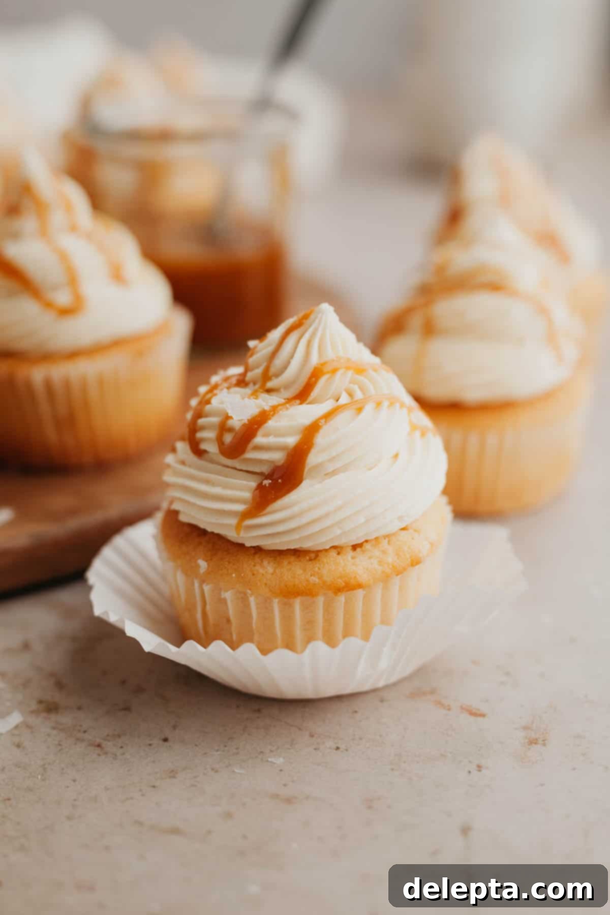 Caramel Burst Cupcakes 13 A caramel cupcake in a white paper liner, topped with buttercream and drizzled with caramel.
