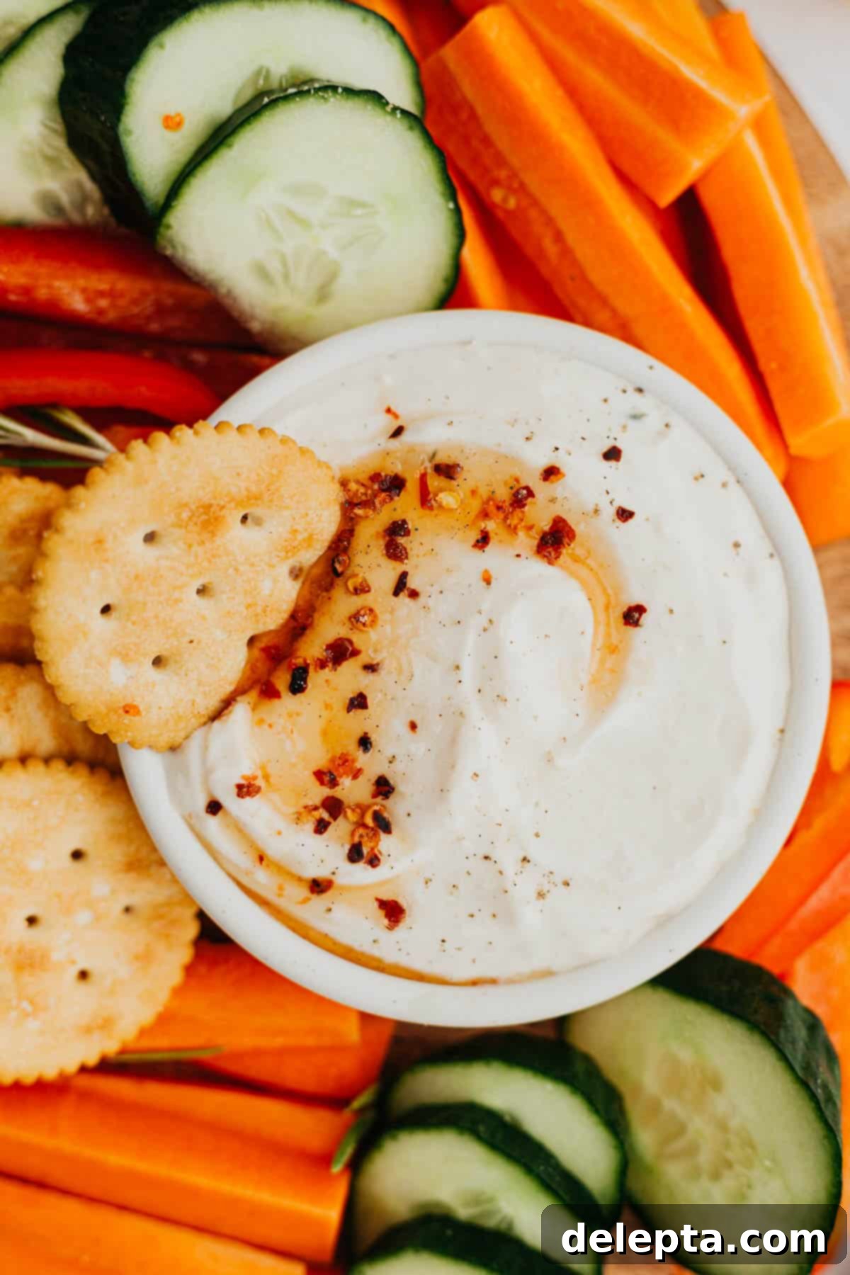 Sweet Heat Ricotta Cloud 2 A white bowl filled with creamy whipped ricotta dip, beautifully drizzled with glistening hot honey and garnished with fresh herbs. The bowl is artfully surrounded by an assortment of vibrant, crisp cut vegetables like carrots, bell peppers, and cucumber slices, alongside crunchy crackers, inviting a delightful snacking experience.