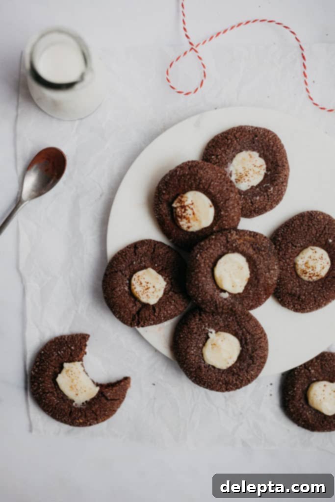 Fireside Cocoa Jewels 2 Several rich chocolate thumbprint cookies with white chocolate ganache, artfully arranged on a elegant marble tray. One cookie features a clear bite mark, revealing its luscious interior.
