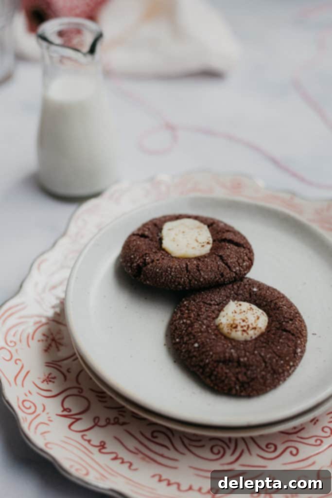 Fireside Cocoa Jewels 4 Two perfect hot chocolate thumbprint cookies on a small white plate, accompanied by a glass of milk, suggesting a delightful snack.