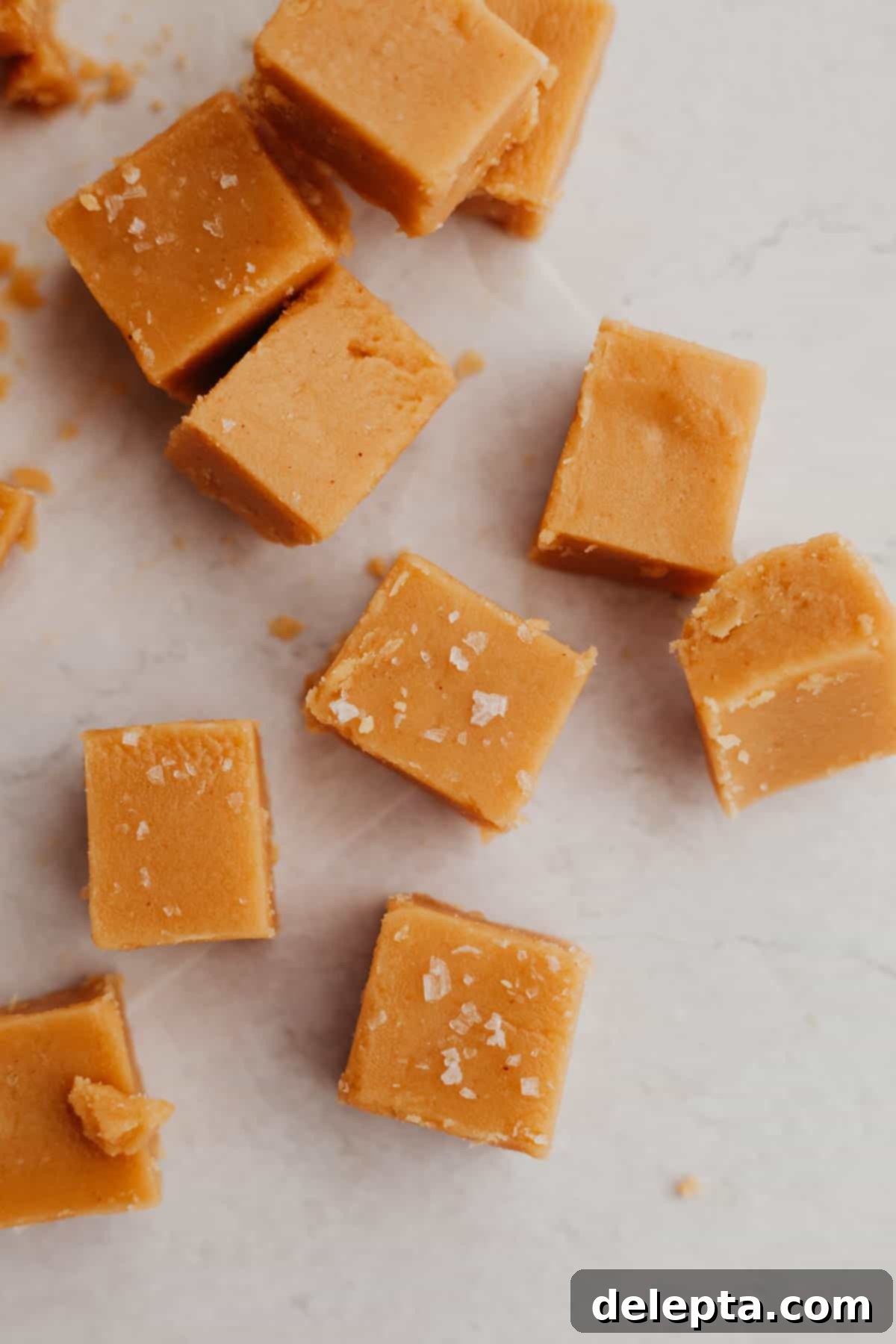 Effortless Peanut Butter Dream 6 A glorious pile of freshly sliced, creamy no-bake peanut butter fudge squares, lightly sprinkled with flaky sea salt, displayed on an elegant marble counter.