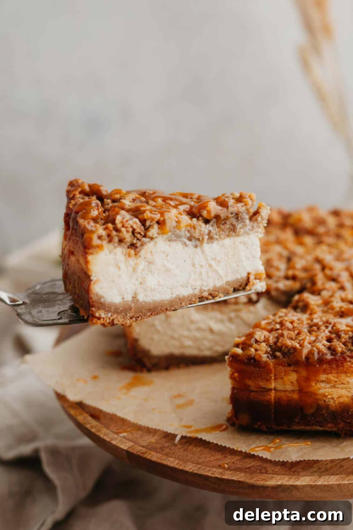 Apple Crumble Cheesecake 11 A beautiful slice of apple crisp cheesecake being lifted out of the whole cake, showing the layers.