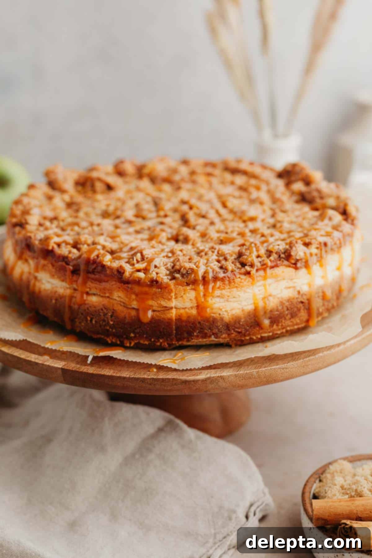 Apple Crumble Cheesecake 10 An apple crisp cheesecake on a wooden cake stand, ready to be served and enjoyed.