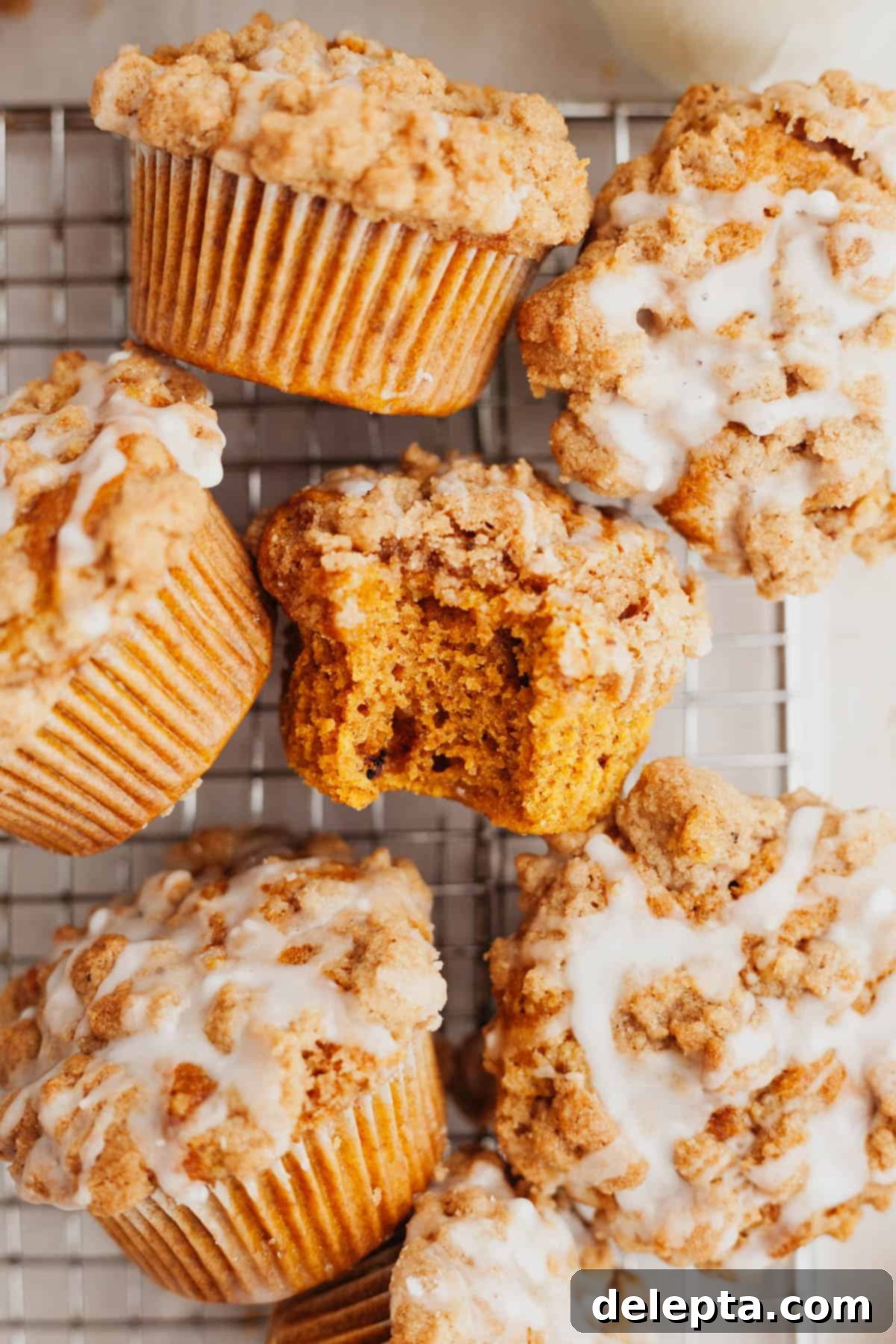 Autumn Spiced Pumpkin Crumble Muffins 7 Several pumpkin muffins drizzled with a white glaze on a wire cooling rack, one muffin has a bite taken out of it.