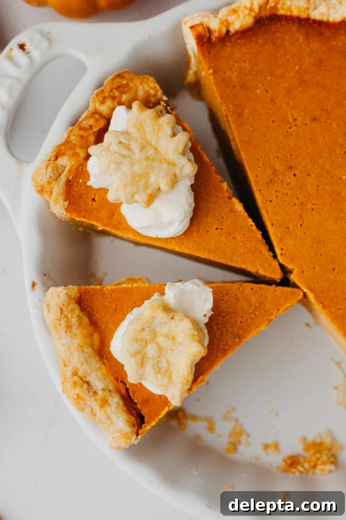 Creamy Pumpkin Dream Pie 7 An overhead view of two slices of pumpkin pie, each generously topped with fluffy whipped cream and served in a cozy setting.